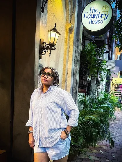 A different pose in the same oversized shirt and shorts outfit, looking up at the cafe sign.
