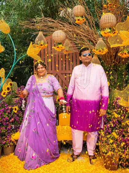 The couple stands in a shower of yellow petals at their sunflower and purple-themed Haldi, a perfect, colorful moment.