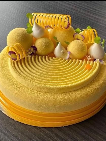 Another example of our sophisticated mousse cakes. This one features a smooth yellow velvet texture with intricate spiral piping and decorative spheres.