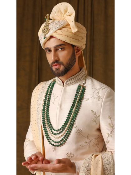 A detailed shot of the 'Jashn-e-Ada' sherwani, highlighting the intricate threadwork with subtle gold hints and the elegant emerald necklace that completes the look.