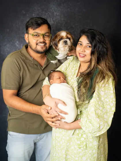 The whole family is here. This portrait includes the new parents, their swaddled newborn, and their beloved dog, showing what a complete family looks like.