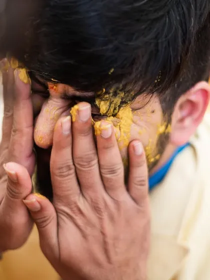 The groom bracing himself as his friends apply haldi.