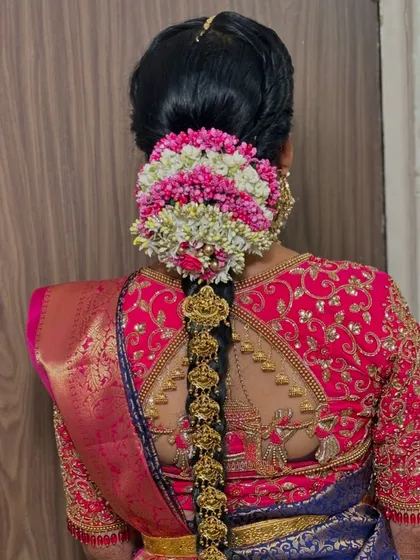 A close-up of the floral bun and the start of the braid. The vibrant colors of the flowers add a beautiful contrast to the bride's dark hair and traditional gold jewellery.