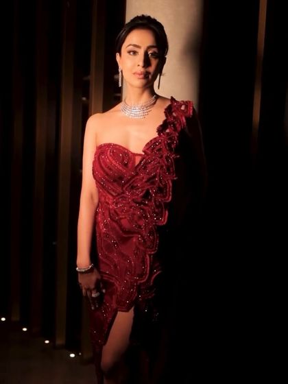 Another angle of the crimson one-shoulder gown, highlighting the detailed embellishment that flows down the body, creating a look of graceful glamour.