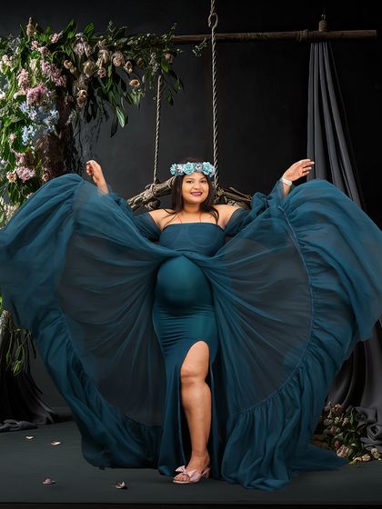 A joyful and dynamic studio portrait of a woman on a swing, her blue gown fanning out around her. The dark floral backdrop and her happy expression make this a truly captivating image.
