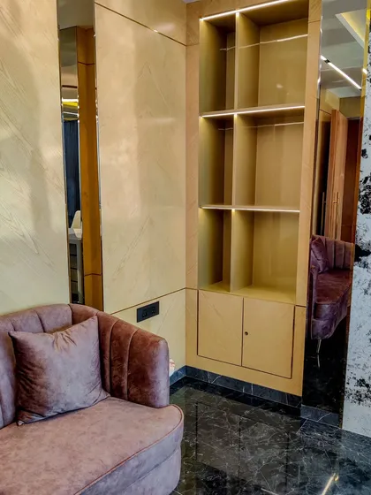 A custom-built shelving unit with integrated lighting, designed for a director's cabin. The combination of wood-grain laminate and mirrored panels creates a sense of space and elegance.