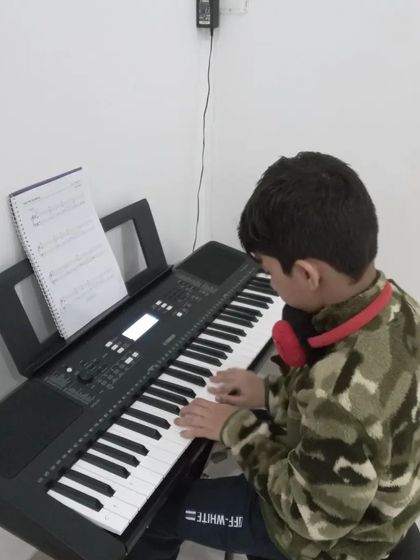 A young student with headphones on, concentrating on his keyboard practice.
