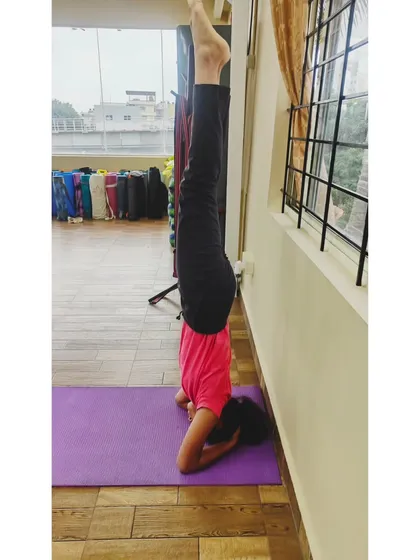 A student holds a steady headstand using the wall for support. This is an excellent way to get comfortable being upside down and build the necessary shoulder and core strength for the full pose.