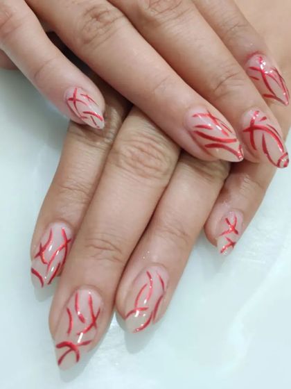 A bold and graphic design with freehand red lines creating an abstract pattern over a sheer nude base on stiletto nails.