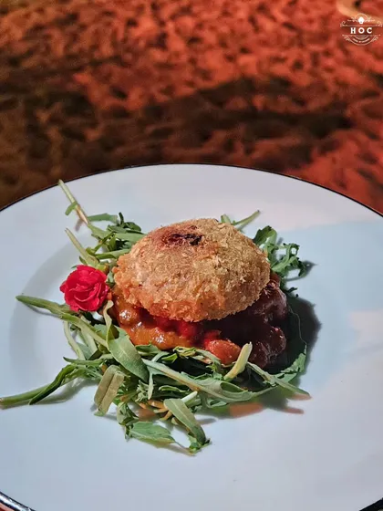 This bite-sized creation features a crispy, breaded patty served on a bed of savory relish and fresh greens. It is a perfect example of how we create complex, multi-layered flavors in a single canapé.