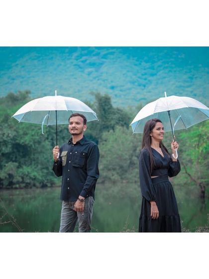 A stylish portrait of a couple holding umbrellas by a serene lake, creating a calm and picturesque pre-wedding photo.