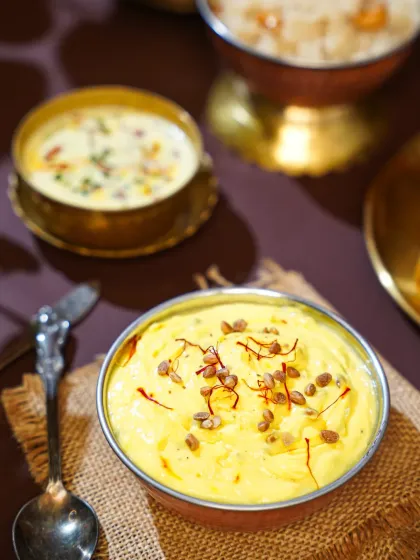 A close-up of creamy, yellow Shrikhand, a traditional Maharashtrian dessert, garnished with saffron and nuts. The soft light and rustic bowl give it a comforting, homemade quality.