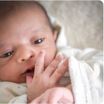 A close-up of a newborn's face, showing their tiny hand and curious eyes.