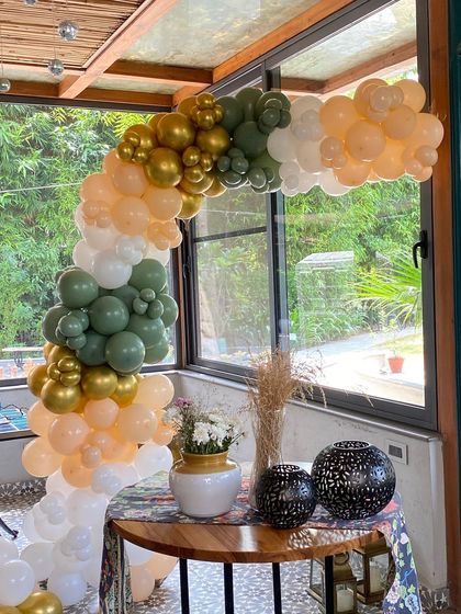 An elegant balloon arch in olive green, peach, and white, perfect for a sophisticated daytime event.