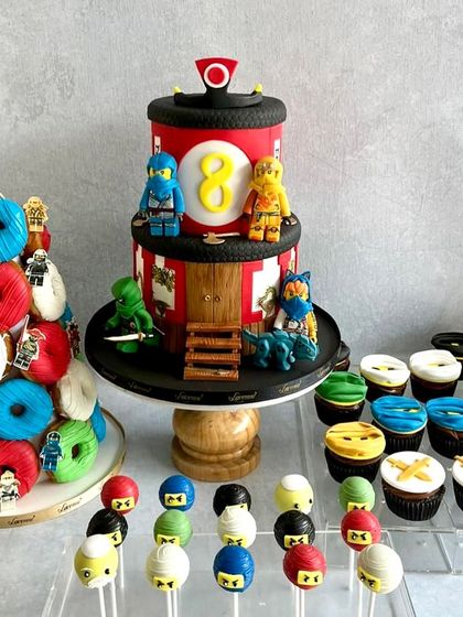 A full Ninjago dessert table for Ved's 8th birthday, complete with a two-tiered cake, a donut tower, and matching cupcakes and cake pops.