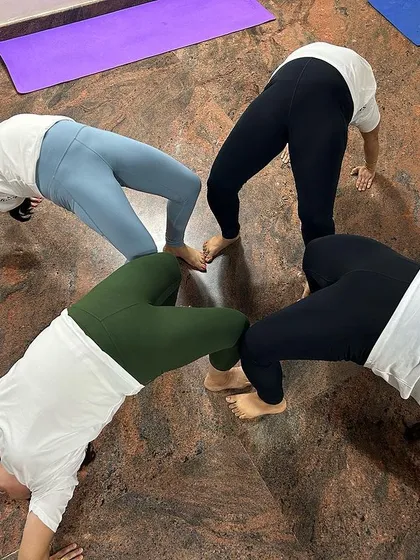 A creative group formation showing four students connecting in a circle through the wheel pose. This not only builds strength but also fosters a sense of unity and shared accomplishment.