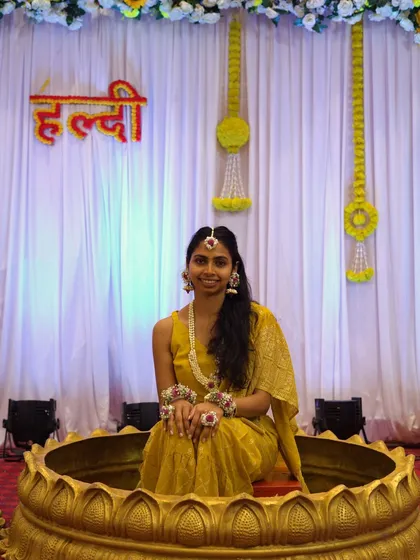A full view of a bride at her Haldi ceremony, seated in a decorative lotus-themed seat. She is wearing a complete handmade floral jewellery set that I designed for her special day.