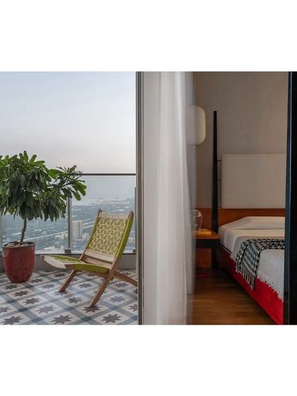 A bedroom balcony in a high-rise apartment, featuring patterned tiles and a comfortable chair. Even in a dense urban setting, I carve out private outdoor spaces that offer a connection to the sky and the city beyond.