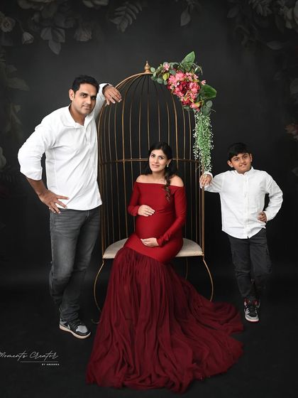 A strong and stylish family portrait. The coordinated white shirts and the mom's bold red gown create a striking contrast against the dark background and birdcage prop.