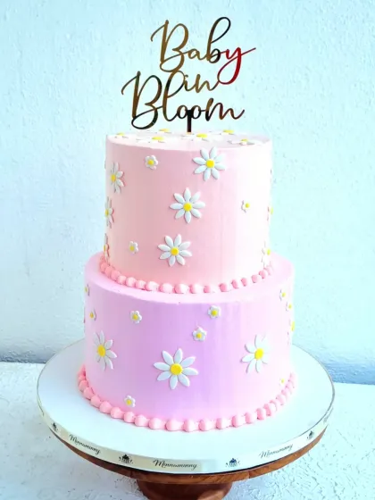 A two-tiered "Baby in Bloom" shower cake with a soft pink buttercream finish. I show how to make these simple but perfect daisy flowers from fondant and how to pipe a neat pearl border.