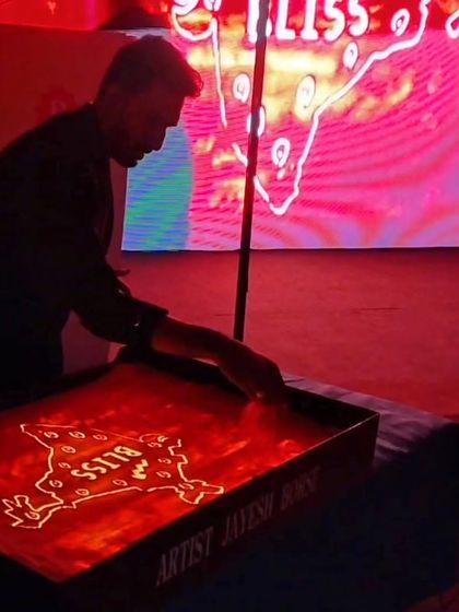 A close-up shot during the Bliss corporate event. The red backlighting creates a dramatic effect as I draw the company's logo and story elements in the sand.
