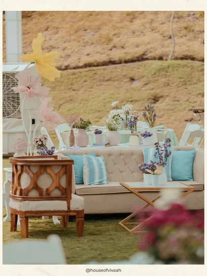 A comfortable lounge setup at the Haldi lunch, with a neutral-toned sofa accented by pastel blue cushions, surrounded by lush greenery.