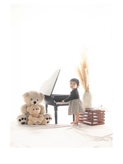 The little musician stands at her piano, looking towards the camera. This shot captures her curiosity and engagement with the fun, themed props in the studio.