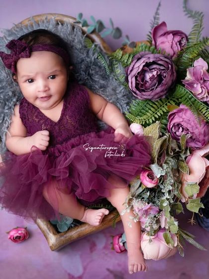 An awake and curious newborn girl in a beautiful purple dress, surrounded by flowers. We capture those precious open-eyed moments too.