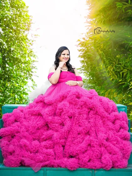 A stunning shot of a mother-to-be in a vibrant pink ruffled gown, seated on green steps. The composition and colors create a visually striking image.