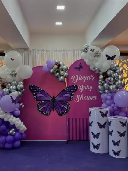 A unique butterfly-themed baby shower for Divya. The purple and silver balloon arrangement complements the custom backdrop and matching pedestals, creating a cohesive and stylish look.