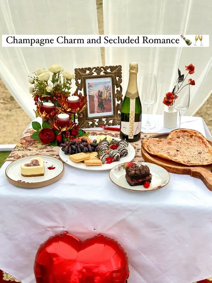 The table is set for a secluded romantic meal. This image highlights the fine details, from the heart-shaped balloon and fresh flowers to the delicious food and champagne, all arranged within a private tent.