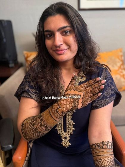A happy bride showing off her full back-of-hand mehendi. The design extends up her arm, creating a complete and cohesive look that is perfect for her big day.