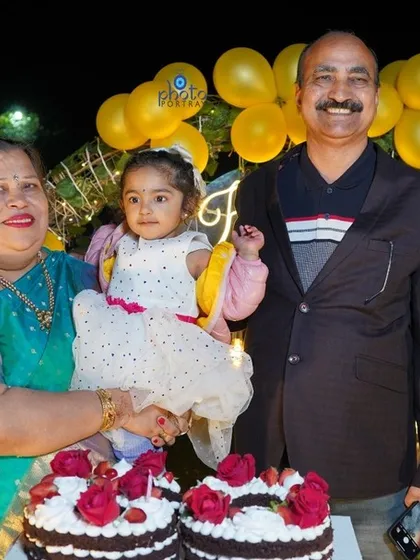 Grandparents and their grandchild pose for a photo by the birthday cakes at a 60th birthday party. My photography captures memories across generations.