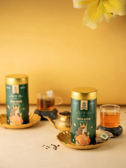 A bright and airy shot of Hindraj's Green Begum tea. The golden background and delicate placement of the tins create a feeling of lightness and elegance, perfectly matching the nature of green tea.