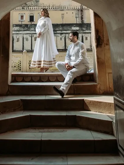 A closer view of the couple framed in the archway, showcasing their elegant, coordinated white outfits against the warm tones of the palace stone.