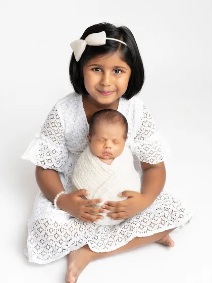 There is nothing more precious than the first moments between siblings. In this simple and clean studio shot, a proud big sister holds her newborn sibling. The focus is entirely on the tender connection and love between them.