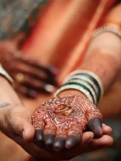 A close-up, artistic shot showing the wedding rings resting in the bride's henna-adorned palm, held gently by the groom. This detailed photograph symbolizes the promise and beginning of a new life together.