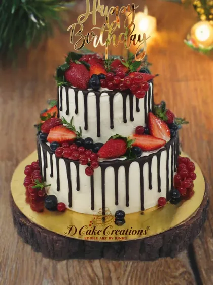 A two-tier birthday cake with a chocolate drip effect, topped with an abundance of fresh berries. The "Happy Birthday" topper makes it a perfect choice for a stylish and delicious celebration.
