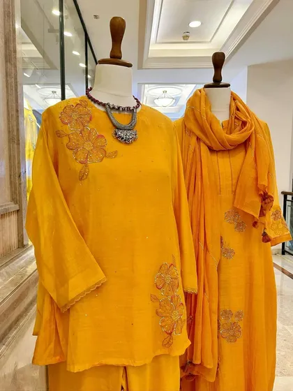 Sunshine in an outfit. This display shows two beautiful yellow kurta sets, one with a matching dupatta and the other a tunic, both adorned with delicate floral embroidery.