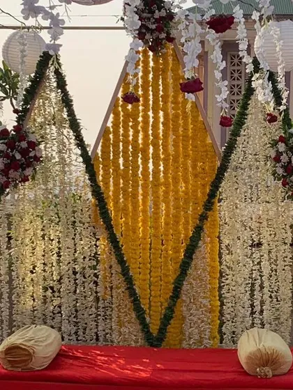 A unique and modern Haldi backdrop with a geometric design. We used curtains of white and yellow flowers to create three distinct panels, offering a contemporary twist on traditional floral decor.