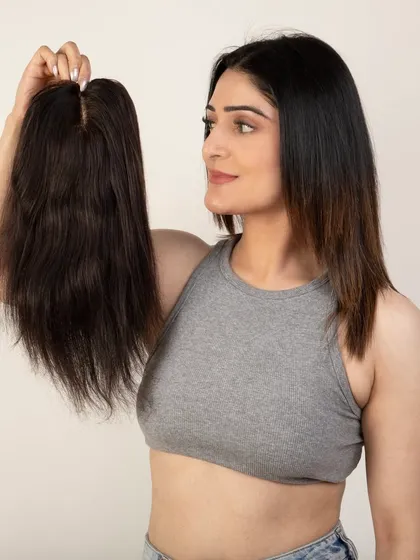 A model holding a smaller hair topper, comparing it to her own hair.