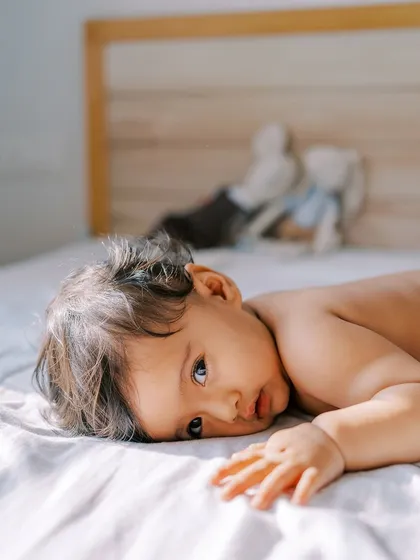 A quiet, thoughtful moment of a nine-month-old baby lying on the bed, bathed in beautiful sunlight.