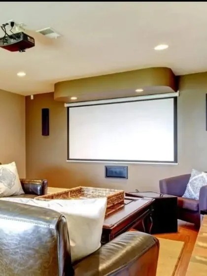 A comfortable and classic living room theater featuring a ceiling-mounted projector, a retractable screen, and in-wall speakers for a surround sound experience without cluttering the floor.