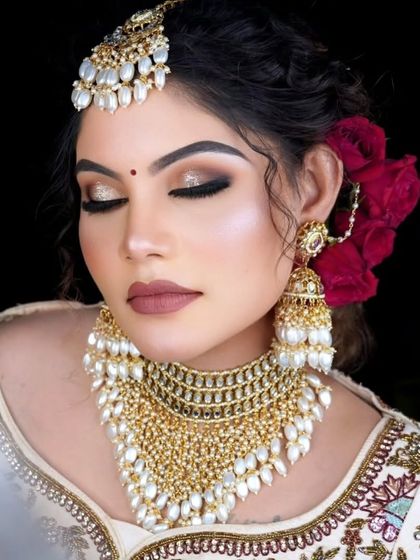 A close up of a bride wearing a gold-plated kundan choker with cascading pearl details. This set is paired with heavy jhumkas and a maang tikka for a complete look.