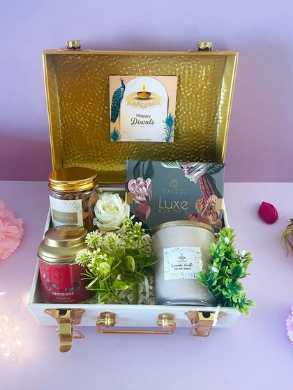This elegant curation in the white and gold metal trunk includes a large scented candle, gourmet nuts, and other premium treats, surrounded by delicate floral accents.