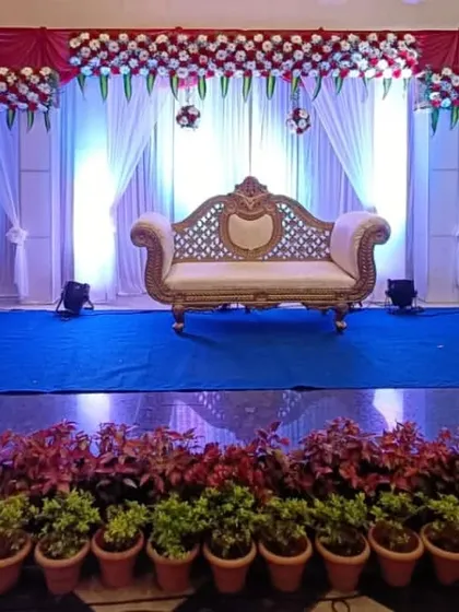 An engagement stage setup with a clean, wide design. This features a red and white floral arrangement across the top, white drapes, and dramatic blue uplighting for a modern feel.