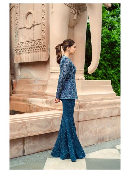 A profile shot of Sharvari in a stunning blue embroidered outfit. The architectural details of the location add a sense of grandeur.