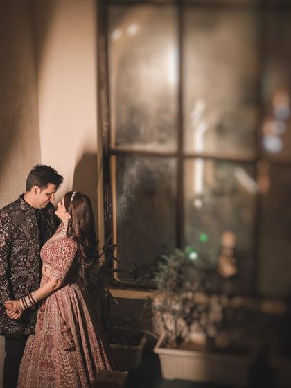 An intimate embrace by a window at night. The soft, ambient light and the reflection in the glass create a cozy and romantic atmosphere for this beautiful pre-wedding portrait.
