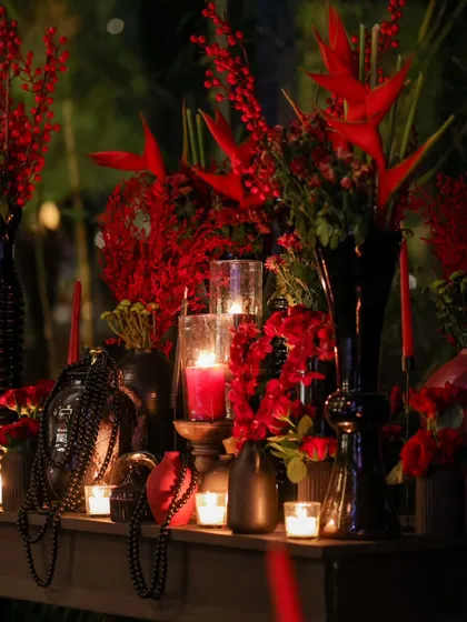 An artful arrangement of red florals in textured black vases, illuminated by candlelight, creating a moody and romantic tablescape.