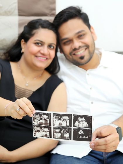 A close-up shot of the couple proudly displaying their sonogram pictures. The focus is on their happy faces and the first images of their baby.